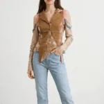 Modella che indossa una camicia innovativa in tonalità marrone con dettagli colorati e maniche lunghe, abbinata a jeans chiari. Sfondo neutro per evidenziare l'outfit moderno e stiloso.