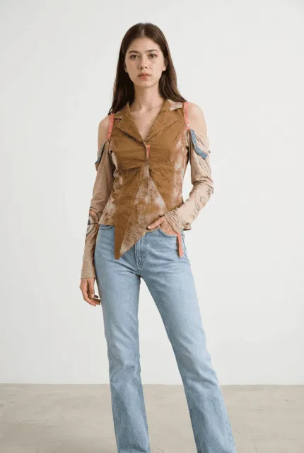 Modella che indossa una camicia innovativa in tonalità marrone con dettagli colorati e maniche lunghe, abbinata a jeans chiari. Sfondo neutro per evidenziare l'outfit moderno e stiloso.