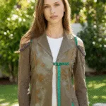 Modella con giacca innovativa in tessuto marrone con dettagli colorati, posata in un ambiente verde e luminoso. La giacca presenta spalle scoperte e chiusure decorative, evidenziando uno stile moderno e alla moda.