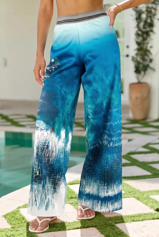 Pantaloni larghi da donna con stampa blu e bianca, indossati con sandali bianchi, in un ambiente estivo vicino a una piscina. Design elegante e fresco, ideale per look casual e vacanze.