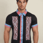Modello maschile che indossa una camicia a maniche corte con un design colorato e moderno, caratterizzata da motivi geometrici e dettagli in blu e rosa.