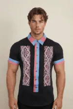 Modello maschile che indossa una camicia a maniche corte con un design colorato e moderno, caratterizzata da motivi geometrici e dettagli in blu e rosa.