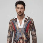 Uomo che indossa una camicia a maniche lunghe con un design artistico e dettagli colorati, in un contesto neutro.