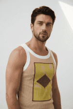 Uomo con canotta beige e grafica colorata, in posa su sfondo neutro, evidenziando uno stile moderno e casual.