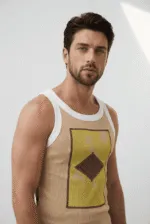 Uomo con canotta beige e grafica colorata, in posa su sfondo neutro, evidenziando uno stile moderno e casual.
