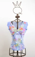 Maglietta blu con stampa floreale su manichino, caratterizzata da un design avvolgente e dettagli colorati. Perfetta per la stagione estiva, con scollatura a V e maniche corte.