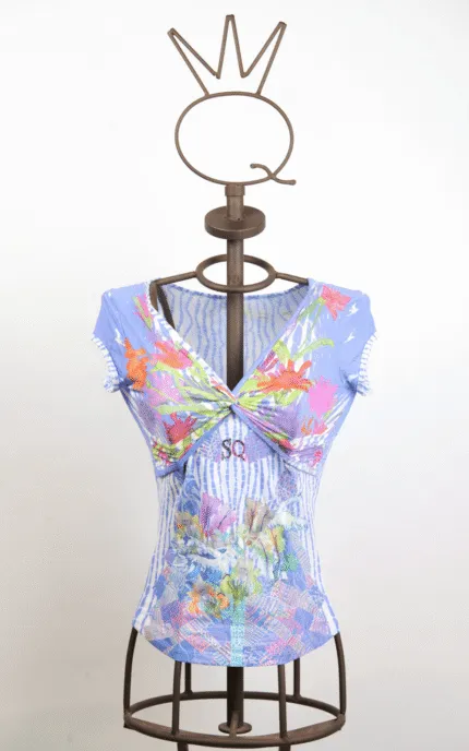 Maglietta blu con stampa floreale su manichino, caratterizzata da un design avvolgente e dettagli colorati. Perfetta per la stagione estiva, con scollatura a V e maniche corte.