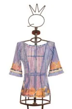 Blusa elegante a maniche lunghe con motivi floreali colorati, presentata su un manichino artistico. Design moderno con dettagli in frange e tonalità di blu e arancione. Ideale per occasioni casual e primaverili.