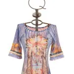 Maglietta colorata con maniche a tre quarti e motivo grafico ispirato alla cultura nativa americana, esposta su un manichino di design. Ideale per un look estivo e informale.