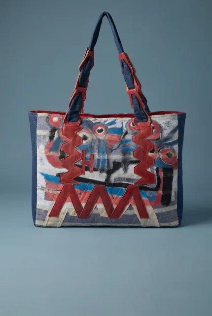 Borsa a spalla colorata con motivi artistici, caratterizzata da manici rossi e dettagli in tessuto blu e bianco, ideale per un look moderno e creativo.