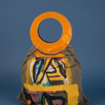 Borsa di design con manico circolare arancione e motivo artistico su sfondo giallo e nero, su un supporto blu. Ideale per uno stile contemporaneo e creativo.