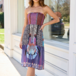 Modella in abito estivo senza maniche, caratterizzato da un design vivace e colorato, posa davanti a una vetrina, evidenziando il tessuto stampato con motivi artistici e una silhouette elegante.