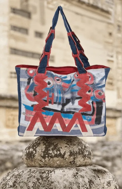 Borsa a tracolla colorata con motivi astratti, appoggiata su una pietra, in un ambiente naturale. Design moderno e creativo, ideale per un look casual e artistico.