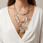 Collana multistrato con pendente colorato a forma di gallo, composta da perline di varie forme e colori, indossata da una donna con una camicia bianca scollata.