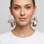 Modella con orecchini a cerchio decorati con animali e fiori, indossando una maglietta bianca. Gli orecchini presentano un design colorato e creativo, evidenziando dettagli come un'anatra e un coniglio.