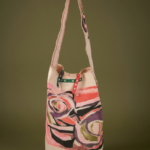 Borsa a tracolla con design artistico, realizzata in tessuto leggero, con motivi colorati e manici a strisce. Ideale per un look casual e moderno.