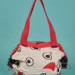 Borsa di stoffa con design creativo, caratterizzata da colori vivaci e motivi astratti, appoggiata su uno sfondo turchese. Ideale per un look casual e alla moda.