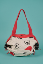 Borsa di stoffa con design creativo, caratterizzata da colori vivaci e motivi astratti, appoggiata su uno sfondo turchese. Ideale per un look casual e alla moda.