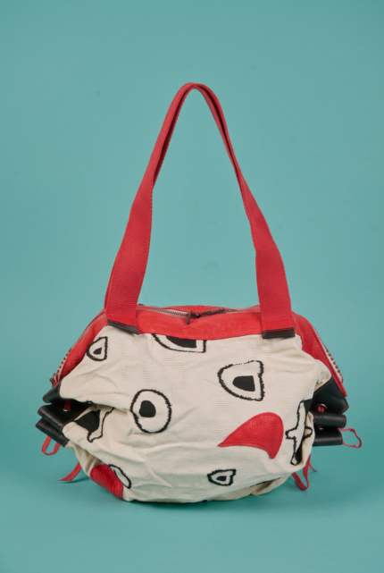 Borsa di stoffa con design creativo, caratterizzata da colori vivaci e motivi astratti, appoggiata su uno sfondo turchese. Ideale per un look casual e alla moda.