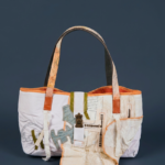 Borsa tote in tessuto bianco con dettagli colorati e manici in pelle, design innovativo e artistico, ideale per un look moderno e casual.