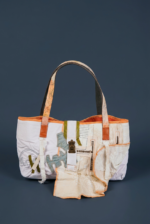 Borsa tote in tessuto bianco con dettagli colorati e manici in pelle, design innovativo e artistico, ideale per un look moderno e casual.