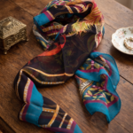 Foulard in crepon di seta con orlo roulotté, caratterizzato da una vivace stampa floreale su sfondo scuro, posato su un tavolo di legno.