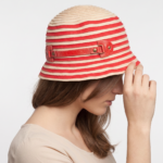 Cappello cloche in cotone a righe rosse e beige indossato da una donna, in primo piano, con le mani che toccano il cappello.