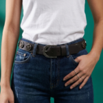 Cintura in vera pelle marrone con borchie e logo indossata su jeans blu, evidenziando la chiusura e il design elegante.