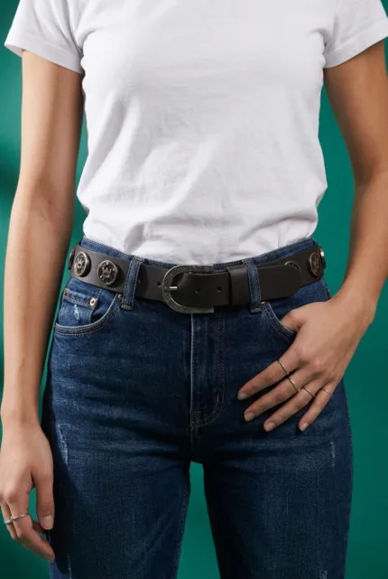 Cintura in vera pelle marrone con borchie e logo indossata su jeans blu, evidenziando la chiusura e il design elegante.