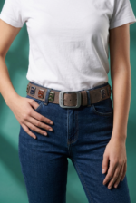 Cintura in vera pelle con bottoni smaltati e maxi fibbia logata indossata da una donna con t-shirt bianca e jeans blu, su sfondo verde.