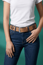 Cintura beige in vera pelle con decorazioni metalliche indossata da una donna, abbinata a jeans blu e maglietta bianca, su sfondo verde.