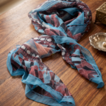 Foulard in crepon di seta con orlo roulotté e stampa colorata, appoggiato su un tavolo di legno, ideale per aggiungere un tocco elegante a qualsiasi outfit.
