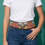 Cintura in tessuto ricamato con dettagli in pelle stampata, indossata da una donna con t-shirt bianca e jeans, su sfondo verde.