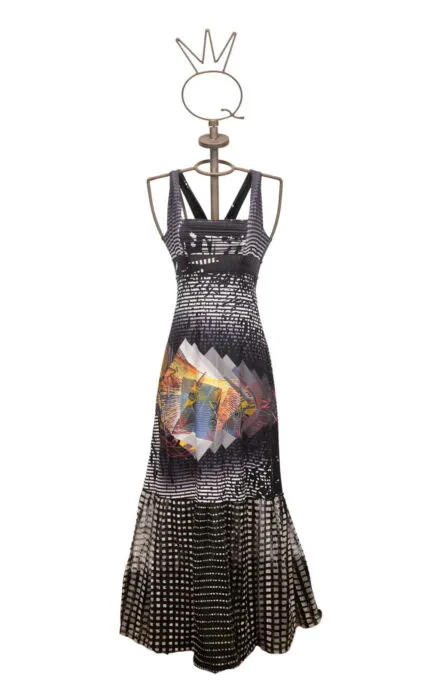 Abito lungo con stampa grafica multicolore, presentato su un manichino elegante. Il design include motivi geometrici e una combinazione di colori vivaci, ideale per occasioni estive.