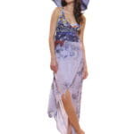 Model wearing a long summer dress with floral pattern and a straw hat, posing on a clear surface. The outfit is elegant and suitable for summer occasions. 
