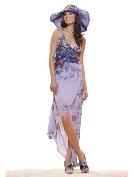 Modella che indossa un abito estivo lungo con motivi floreali e un cappello di paglia, posando su una superficie chiara. L'outfit è elegante e adatto per occasioni estive.
