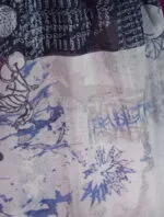 Detail of a lightweight fabric with abstract patterns in shades of blue and pink, featuring artistic lettering and stylized designs, ideal for summer wear or fashion accessories.