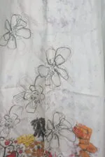 Tessuto con disegni floreali in bianco e nero su sfondo chiaro, evidenziato da dettagli colorati di frutta. Ideale per moda e design tessile.