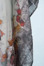 Scialle elegante in tessuto leggero con motivi floreali e fruttati, caratterizzato da tonalità vivaci di rosso, giallo e grigio. Perfetto per un look estivo e alla moda.