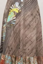 Gonna lunga con stampa artistica, caratterizzata da un motivo di uccello colorato su sfondo marrone e dettagli a strisce. Design unico e vivace che combina elementi naturali e colori brillanti.