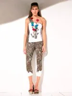 Modella in abbigliamento estivo, indossando un top bianco con decorazioni e leggings a motivi geometrici. Collana colorata e sandali eleganti completano il look. Sfondo neutro.