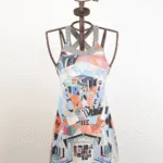 Abito estivo colorato con stampa geometrica e motivi artistici, presentato su un manichino. Ideale per occasioni casual e vacanze, con spalline incrociate e dettagli vivaci.