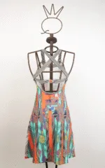 Abito estivo colorato con motivi geometrici e floreali, esposto su una gruccia in metallo con design originale. Il vestito presenta spalline incrociate e una silhouette a trapezio, ideale per occasioni casual.