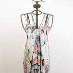 Abito estivo multicolore con spalline, esposto su un manichino. Il design presenta una combinazione di motivi geometrici e floreali, perfetto per occasioni informali e calde giornate estive.