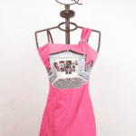 Abito rosa con spallina unica e stampa grafica, esposto su un manichino con supporto a forma di corona. Perfetto per look estivi e casual.