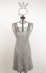 Abito a righe bianche e nere su manichino, con spalline colorate. Design elegante e moderno, ideale per occasioni estive.