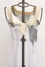 Top in tessuto leggero con dettagli in rete nera e drappeggio bianco, esposto su un manichino. Design moderno e creativo, ideale per look estivi e casual.