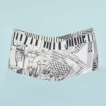 Bermuda shorts swimsuits with black and white graphic print, featuring patterns inspired by musical notes and abstract designs, on a light blue background. Ideal for summer activities and water sports. 