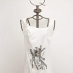 Top bianco con dettagli grafici neri, presentato su un manichino con testa a forma di corona. Ideale per un look casual e alla moda.