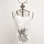 Top bianco con dettagli grafici neri, presentato su un manichino con testa a forma di corona. Ideale per un look casual e alla moda.